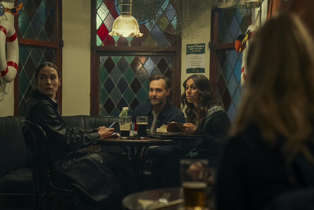 Siobhán Cullen, Will Forte, and Robyn Cara sit at a small bar table in the Netflix series 'Bodkin'