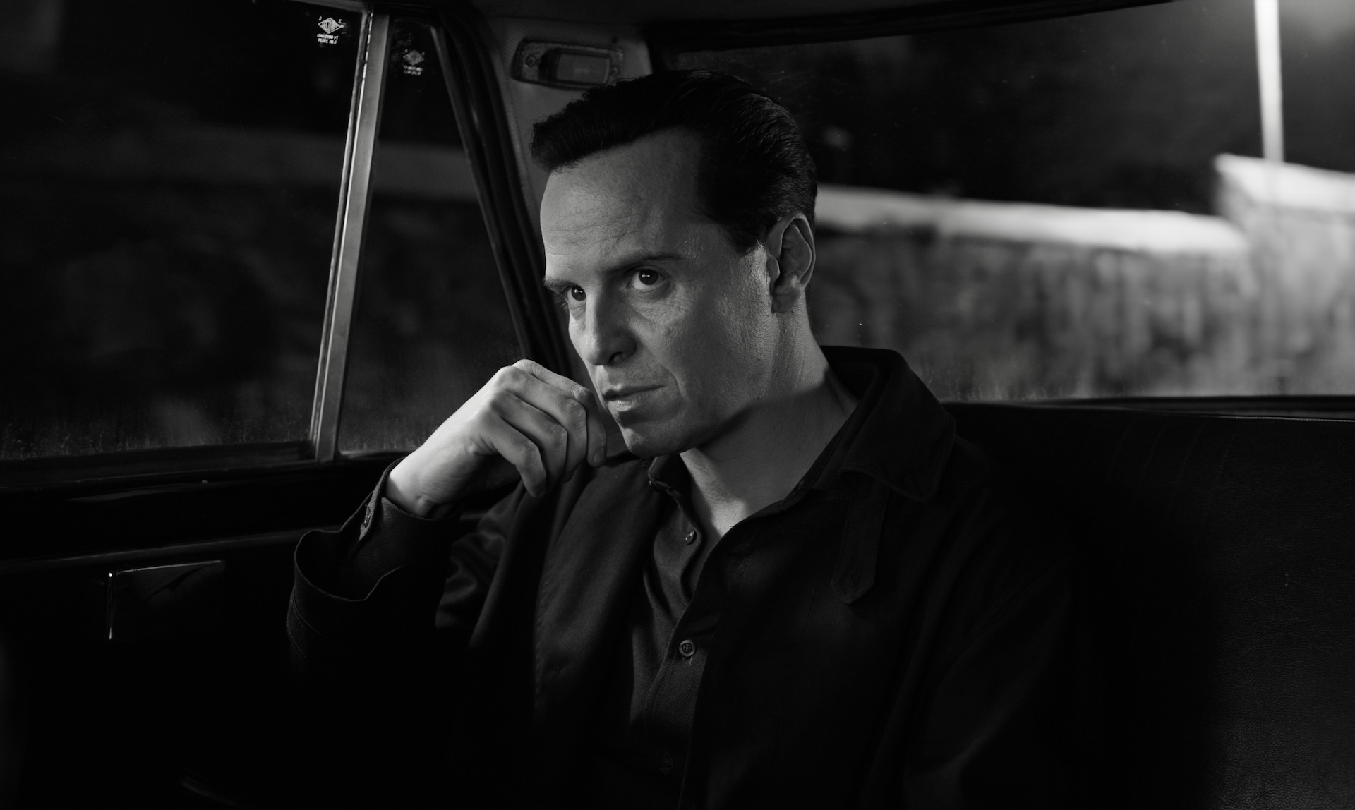 Black-and-white still of a man sitting in the back of a car; Andrew Scott in and as 'Ripley.'