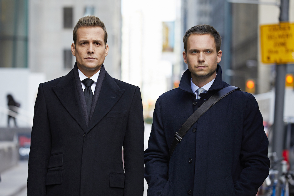 SUITS stars Gabriel Macht as Harvey Specter, Patrick J. Adams as Michael Ross, shown here standing side by side on a city street wearing coats